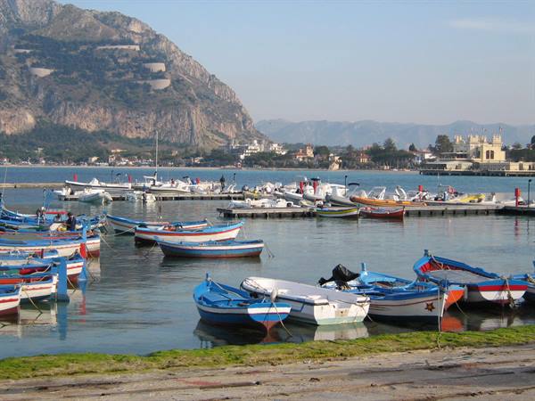 Blue painted wooden boats moored at Mondello harbor beneath the rocky mountain