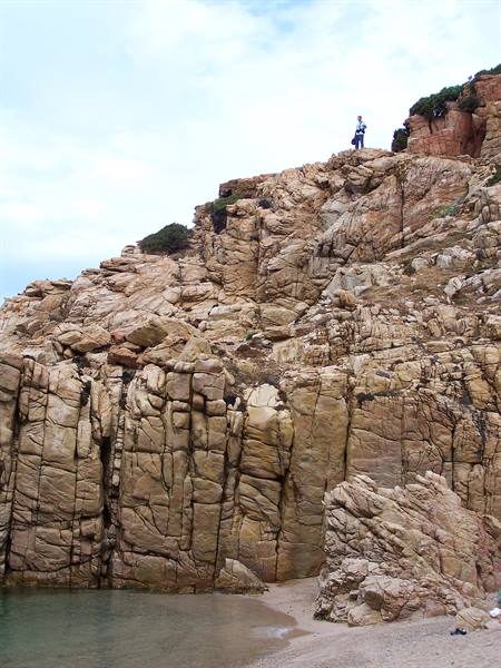 Tourist standing on red granite cliffs above a small sandy beach
