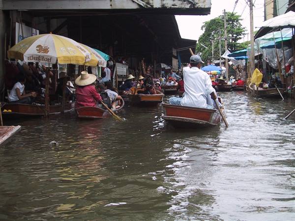 Boatmen paddle wooden boats through the busy Damnoen Saduak floating market