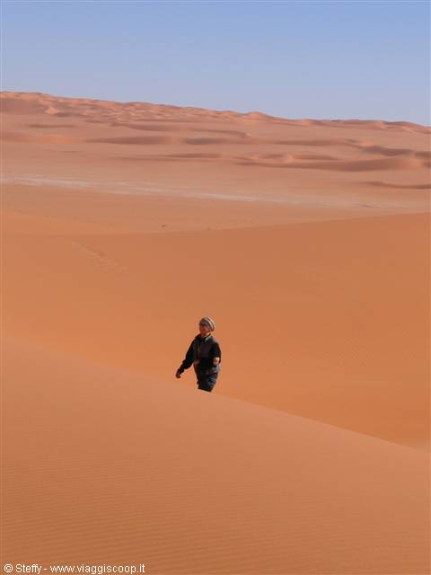 Man in headscarf walks up an orange sand dune in the Sahara desert