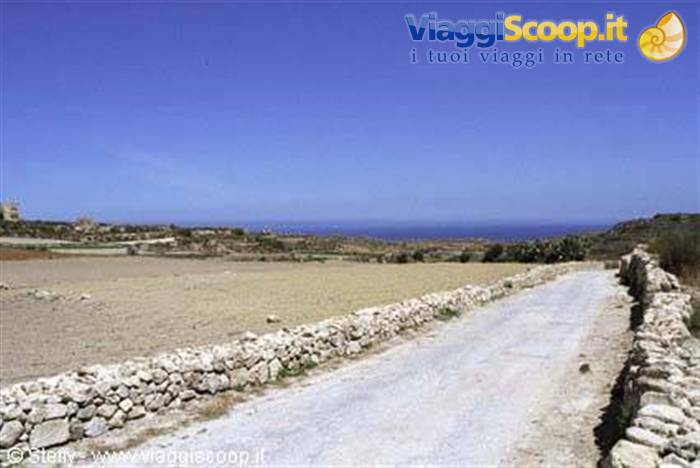 White dirt road between dry stone walls, plowed fields and blue sea ahead