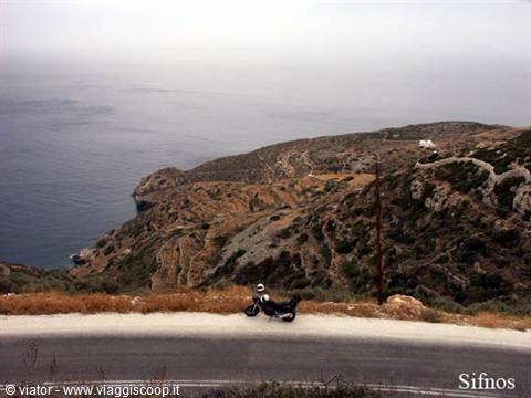Motorbike parked on a coastal road, arid hills and grey sky over Sifnos