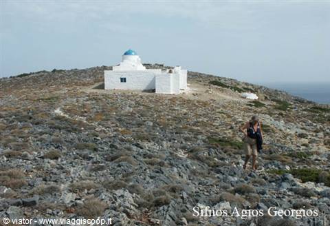Hiker walks across rocky hill toward white Agios Georgios chapel, Sifnos