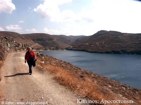 Woman in red jacket walks the coastal dirt track at Apocroussi, Kithnos