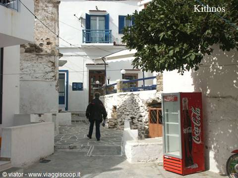 Man walks through whitewashed alley in Chora, Kithnos, beside a Coca-Cola fridge