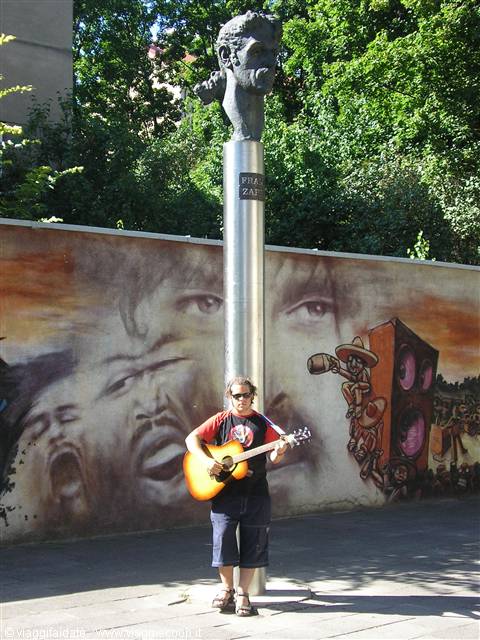Guitarist beneath the Frank Zappa bust in Prague, before a painted mural