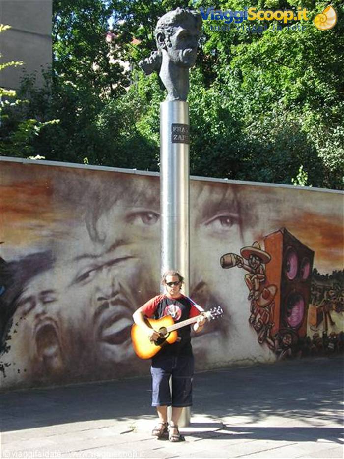 Guitarist beneath the Frank Zappa bust in Prague, before a painted mural