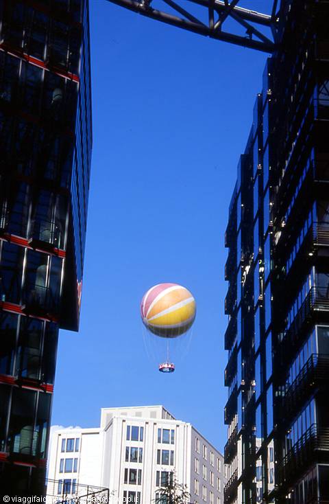Yellow and red balloon floats between glass towers under blue sky