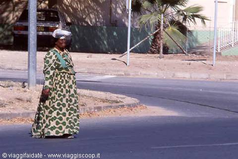 Woman in spotted green dress crossing the asphalt road near palm trees
