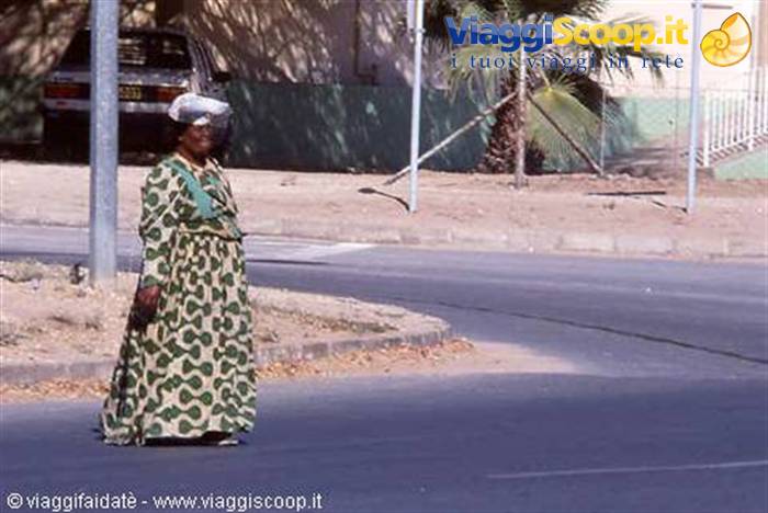 Woman in spotted green dress crossing the asphalt road near palm trees