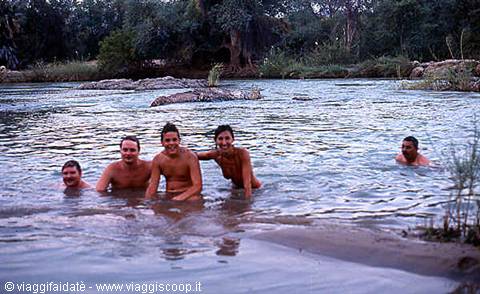 Group of friends in swimwear bathing in a river among rocks and greenery