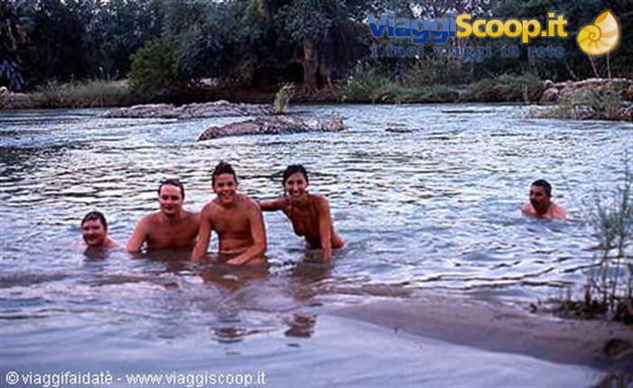 Group of friends in swimwear bathing in a river among rocks and greenery