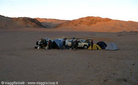 Camp with tents and off-road vehicles among sandy dunes at dawn