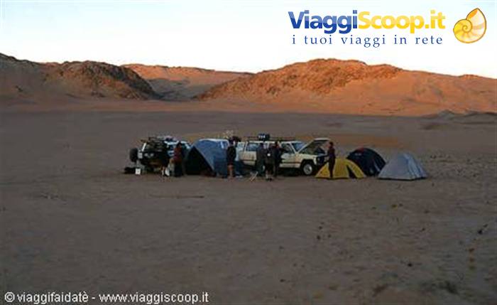 Camp with tents and off-road vehicles among sandy dunes at dawn