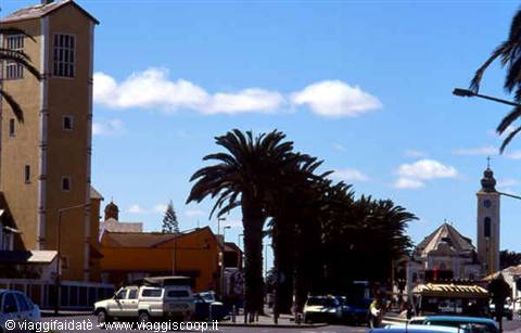 Palm-lined street, yellow tower and church with spire, cars passing by