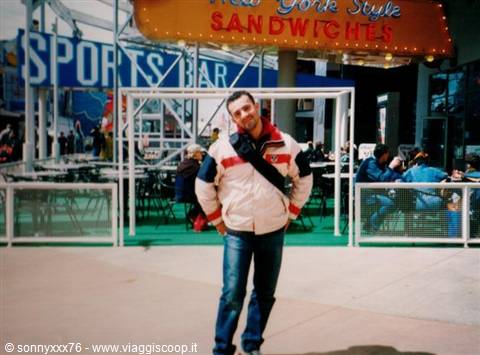 Man in color-block jacket in front of a sandwich stand and sports bar