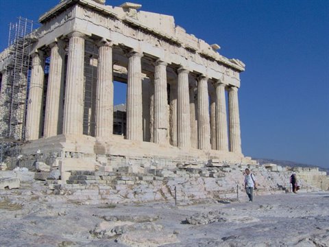 Tourist walks past the Parthenon, marble columns under a blue sky