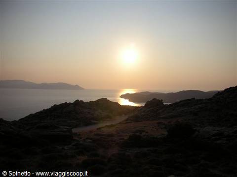Low sun over the sea between dark rocks and arid hills, golden reflection on water