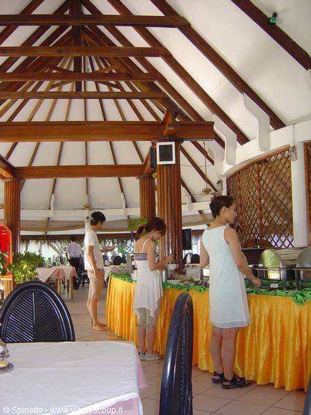 Women serving themselves at a buffet under a wooden-beamed pavilion