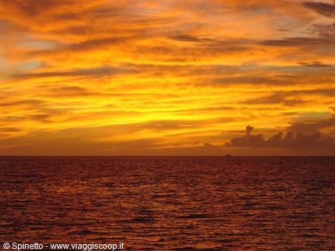 Fiery orange sky over calm sea, a small boat on the horizon