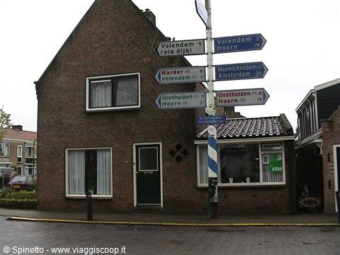 Blue direction signpost beside a brick house under an overcast sky