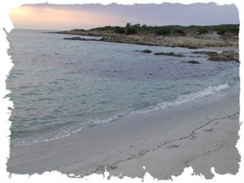 Pale sand beach, gentle waves and granite rocks under a pink sky