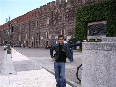 Young man leaning on a stone wall in front of Castelvecchio's crenellated walls, Verona