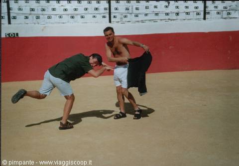 Two young men joking around inside a sandy arena with red barrier