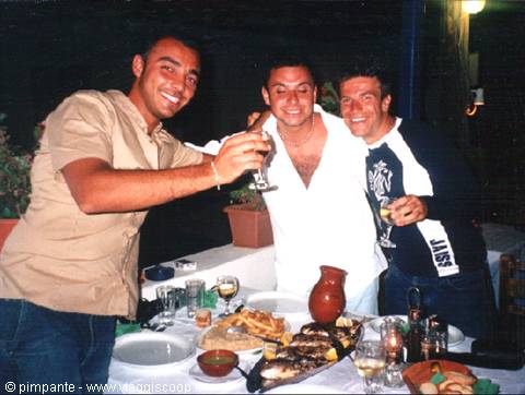 Three friends toast with wine at a table full of grilled fish, night terrace