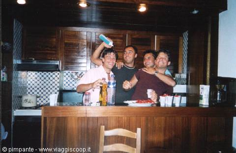 Four friends at a wooden bar, one raising a bottle, drinks and snacks