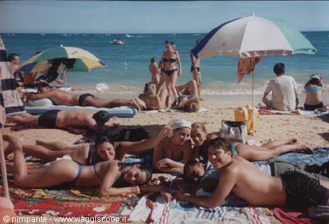 Group of friends lying on the sand under beach umbrellas, crowded shore