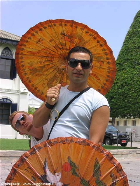 Tourist in sunglasses holding a painted orange parasol in front of a white building