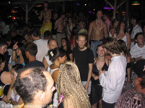 Young crowd dancing at a crowded open-air nightclub, shirtless man on table