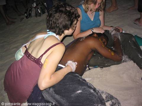 Two girls help an injured man lying on the sand at night
