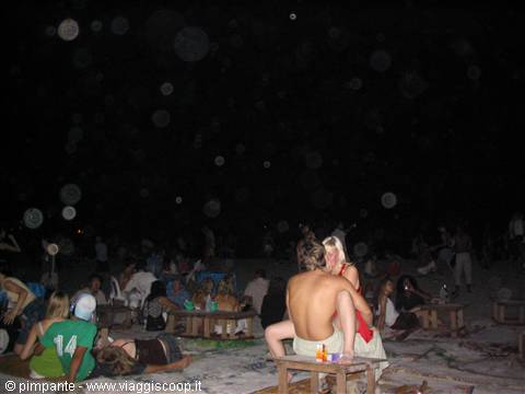 Couple embracing at night on the beach, low wooden tables with drinks