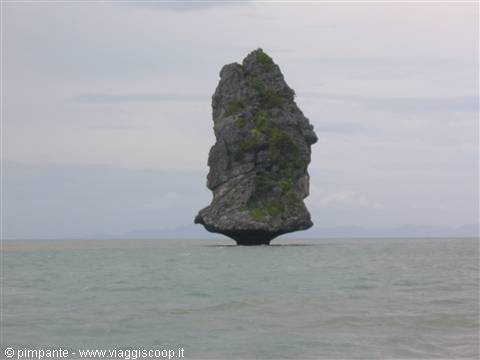 Limestone rock formation rises from calm sea under grey sky