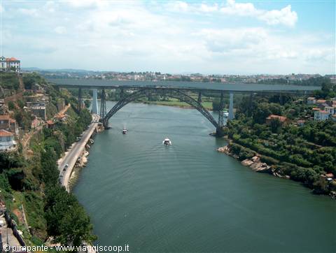 Steel arch bridge spanning the Douro river, boats below, Porto houses among greenery