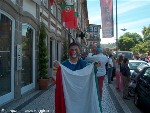 Football fan with painted face holds Italian flag on street with Portuguese flags