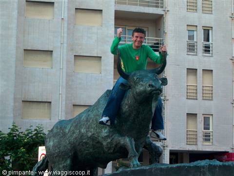 Man in green shirt riding the bronze bull statue in front of a building