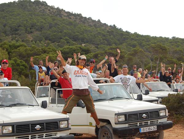 Cheering tourists on white jeeps among green hills, guide jumping in front