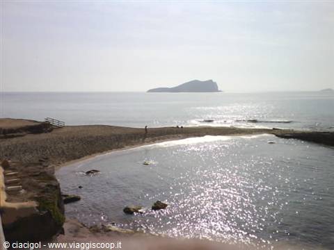 Sandy beach with rocks, sunlight reflecting on the sea, island on the horizon