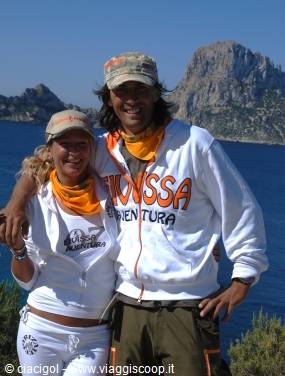 Couple in orange bandanas smiling before limestone cliffs and blue sea