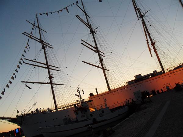 Three-masted tall ship moored at the pier, signal flags strung between masts at dusk