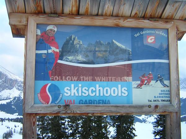 Wooden sign for Val Gardena ski school among snow and Dolomites
