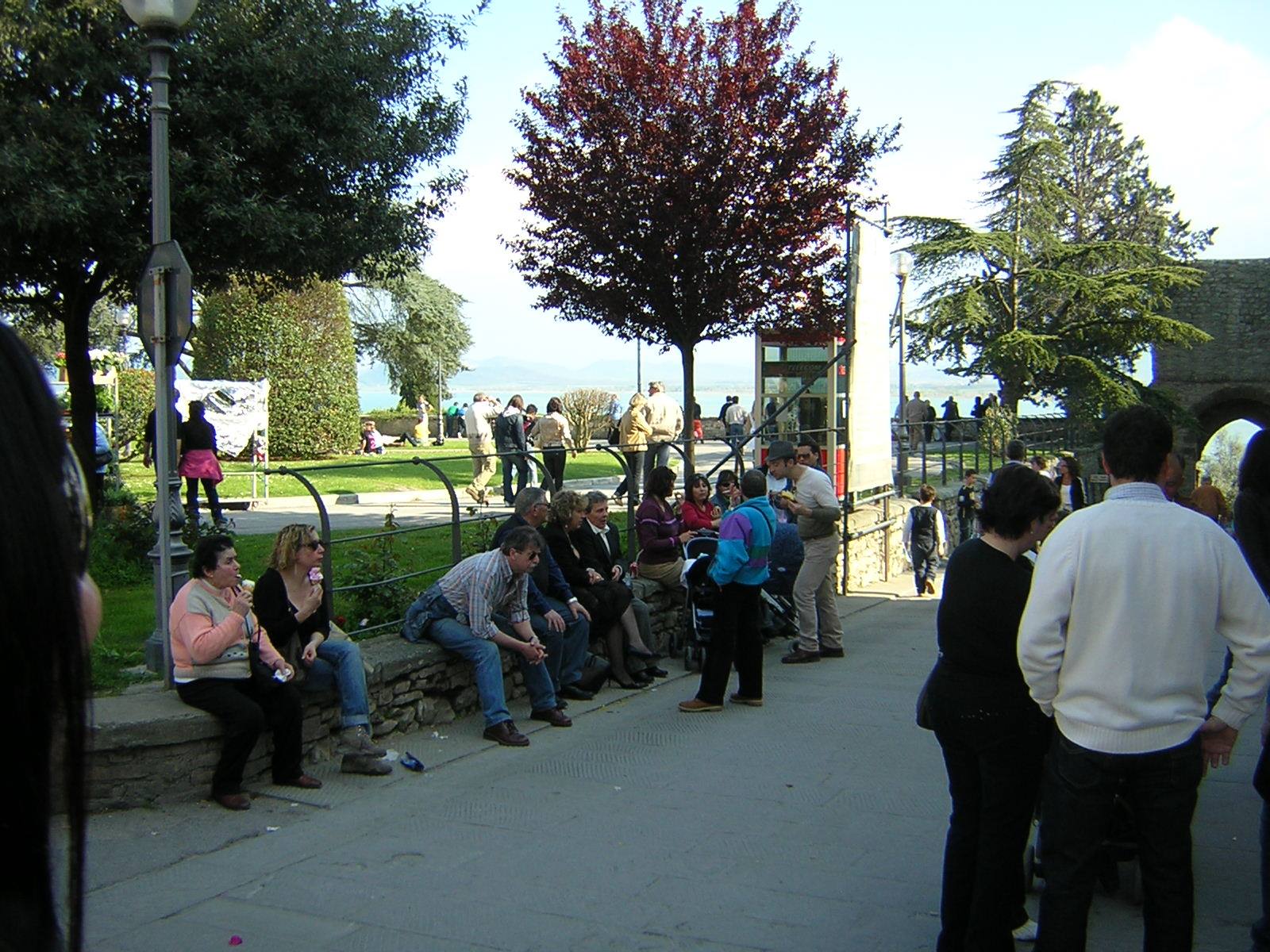 Tourists sitting on a low stone wall in a lakeside park