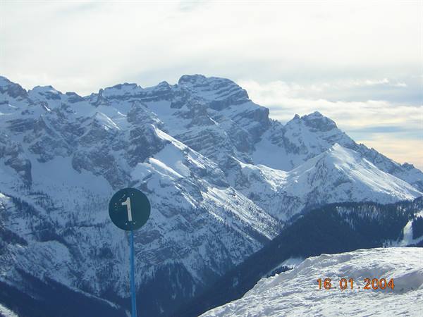 Green sign number one on snowy slope, jagged Dolomite peaks under clouds