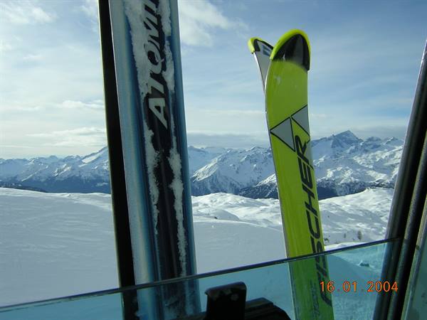 Snow-covered Fischer and Atomic skis inside the gondola cabin among snowy peaks