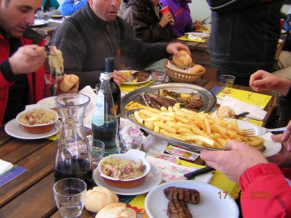 Mixed grill and fries on wooden table, friends eating lunch at mountain hut