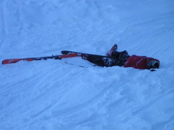 Skier in red jacket fallen in deep snow, red skis beside him