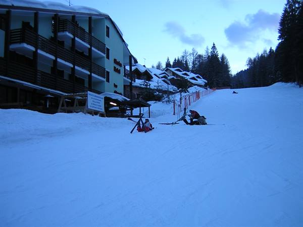 Skiers carrying their gear on the snowy slope in front of a hotel